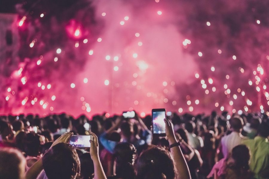 A music festival is seen with a large crowd. https://www.pexels.com/photo/people-taking-photo-of-the-fireworks-3052448/