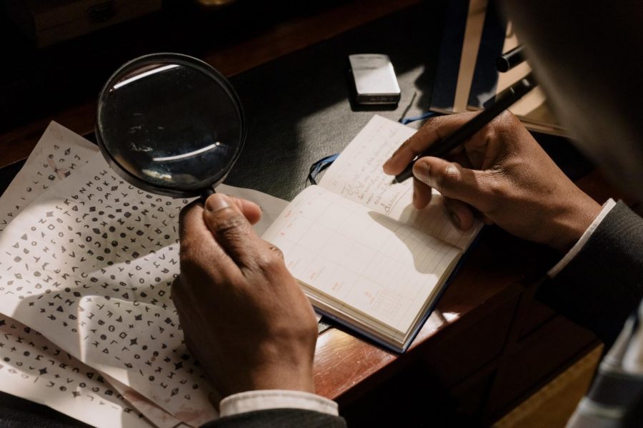 A person is seen taking notes and using a magnifying glass to examine papers. 
https://www.pexels.com/photo/photo-of-person-taking-down-notes-7319070/