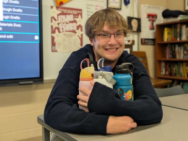 Senior Luke Petersen sheepishly holding multiple, large reusable water bottles.