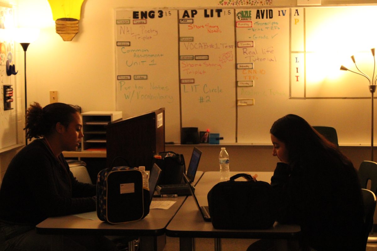Senior Bella Byrom and Areli Mejia work in a lamp-lit environment.